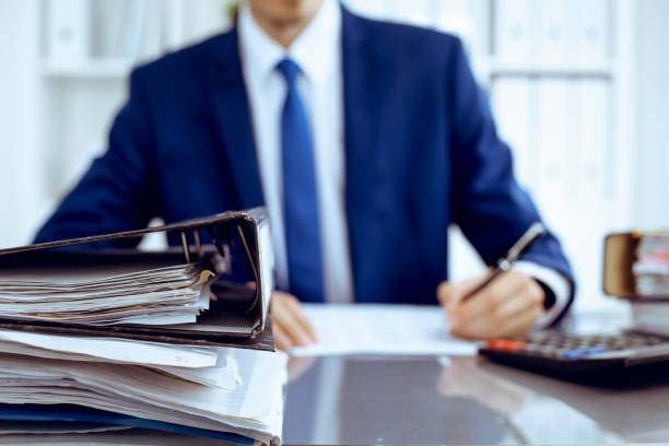 istock Binders with papers waiting to be processed with businessman or bookkeeper back in blur. Accounting planning budget. Audit, insurance and business concept 1176148382