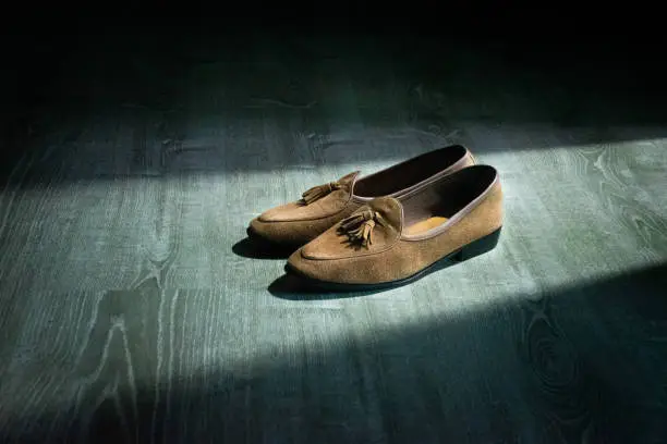 Brown calf suede tassel loafer with wooden background.