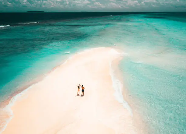 Young adult couple standing on a sandbank against turquoise water in Maldives