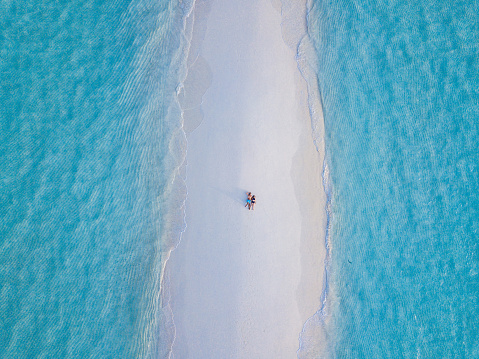 Young adult couple lying together on a sandbank against turquoise water in Maldives