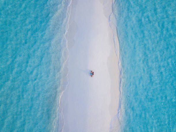 Young adult couple lying together on a sandbank against turquoise water in Maldives Young adult couple lying together on a sandbank against turquoise water in Maldives sandbar stock pictures, royalty-free photos & images