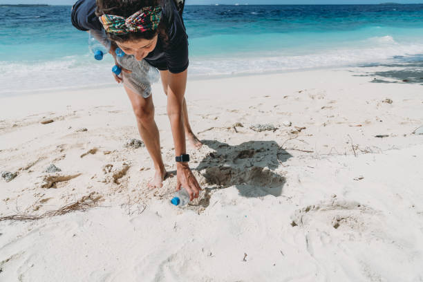 giovane donna adulta che raccoglie alcune bottiglie di plastica abbandonate sulla spiaggia - trash day foto e immagini stock