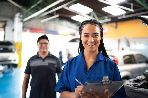 retrato de mujer mecánica automotriz con el cliente en el fondo en el taller de reparación de automóviles - working smiling equipment car fotografías e imágenes de stock