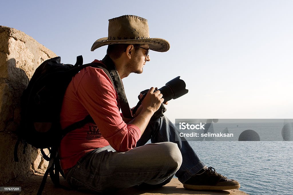 Portrait de jeune photographe tenant la caméra avec un chapeau par la mer - Photo de Hommes libre de droits