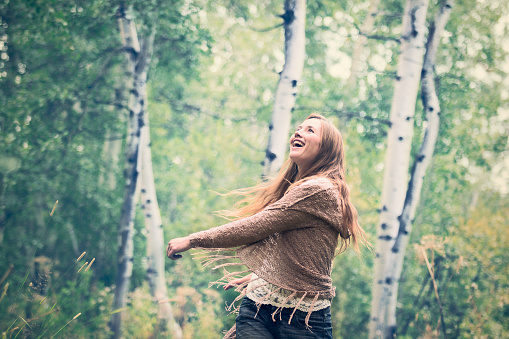 A young woman dancing with joyful expression in a beautiful forest woodland. Color photograph taken in Northern Montana.