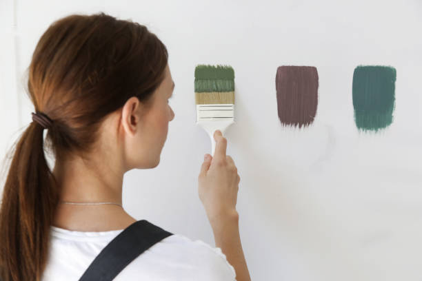 女性は異なる色の見本で壁をペイントしています。壁にぴったりの色を選ぶプロセス、diyホームリフォームのコンセプト。	 カテゴリ 人々 - female house painter home decorator paintbrush ストックフォトと画像