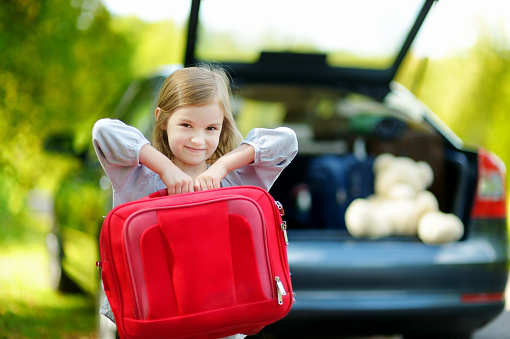 Adorable little girl with a suitcase leaving for a car vacation with their parents