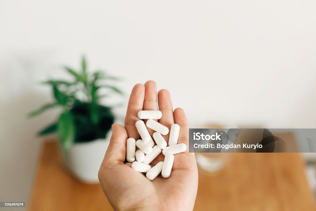 White pills. Dietary supplements.Hand holding magnesium capsules above glass of water on wooden table.  Health support and treatment. Biologically active additives Magnesium Stock Photo