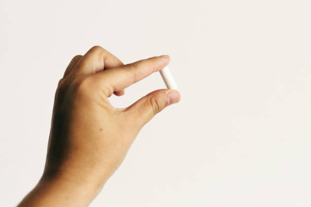 istock Hand holding magnesium capsule on white wall background. Dietary supplements. Health support and treatment. White pill. Biologically active additives 1176199259