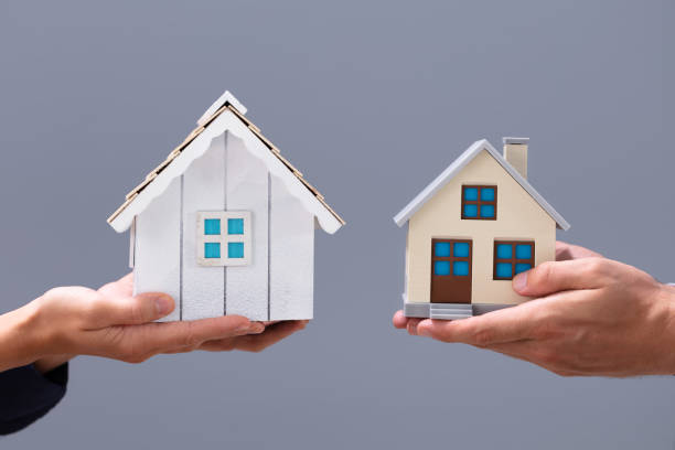 Close-up Of Couple's Hand Holding Different Miniature Houses Close-up Of Couple's Hand Holding Different Miniature Houses Against Gray Background exchanging stock pictures, royalty-free photos & images
