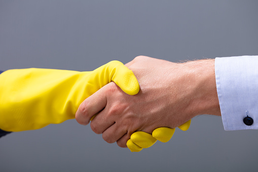 Close-up Of Businessman And Janitor Shaking Hands Together Against Gray Background