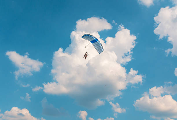 Two men are flying in the blue sky using a colorful parachute