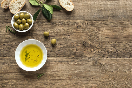 Olive Oil. Organic olive oil with rosemary and green olives in bowl on wooden background with copy space, healthy food concept.