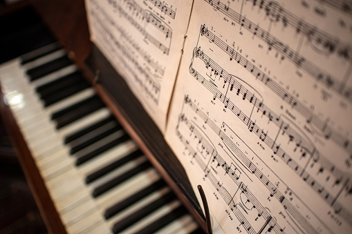 Looking down onto out of focus piano keys with sheet music in the forground