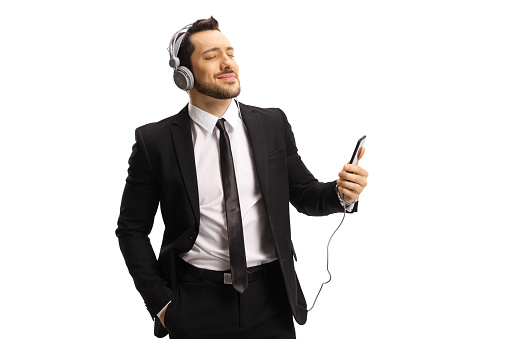 Young man in a suit listening to music on headphones from a mobile phone and enjoying isolated on white background