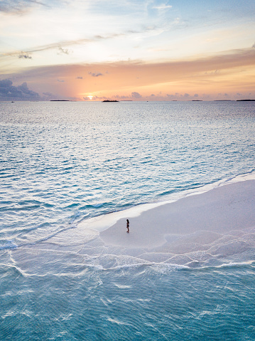 Young adult woman standing on a sandbank against turquoise water in Maldives at sunset