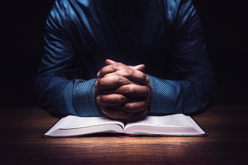 Man praying on a wooden table with an open Bible.