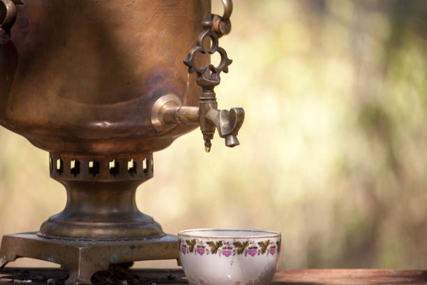 Vintage bronze samovar wood burning and cup on rusty table outdoor, preparing water for tea brewing, selective focus