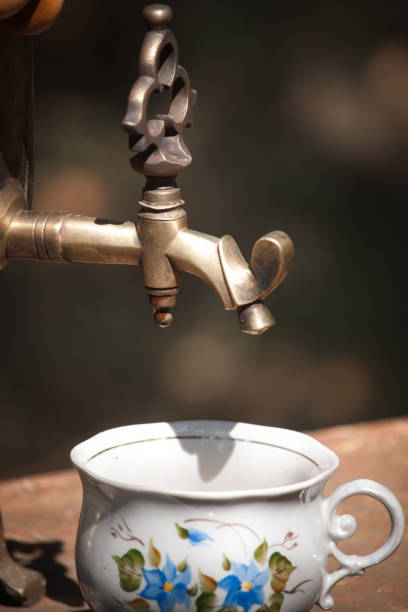 Vintage bronze samovar wood burning and cup on rusty table outdoor, preparing water for tea brewing, selective focus