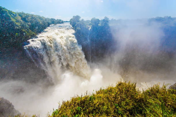 Silhouette of a couple standing together under an umbrella looking at Victoria Falls Mosi-oa-Tunya at sunrise Zimbabwe Africa