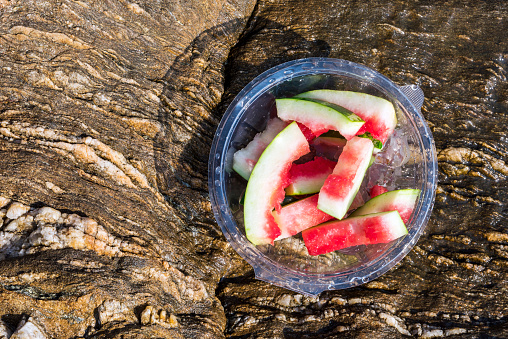 Watermelon peels in plastic container left on rock in Greece.