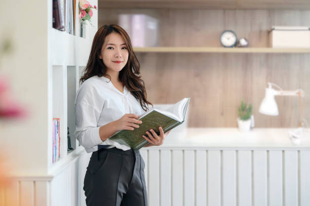 ładna kobieta trzymająca książkę i stojąca w biurze. - report reading business book zdjęcia i obrazy z banku zdjęć
