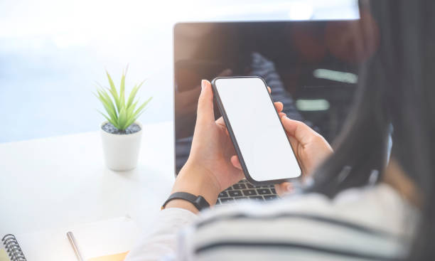istock Closeup view young woman holding smartphone with blank screen while working with laptop.Closeup view young woman holding smartphone with blank screen while working with laptop 1176253971