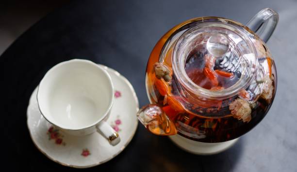 dufttee mit goji (chinesische wolfsbeeren) in transparenten glas teekanne und porzellantasse mit blumenmuster untertasse auf schwarzem tisch top-ansicht - jasmine tea black tea tea drink stock-fotos und bilder