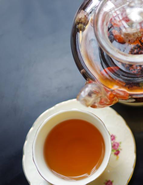 thé noir parfumé avec goji (baies de loup chinoises) et jasmin dans la théière en verre transparente et tasse de porcelaine avec la soucoupe de modèle de fleur sur la vue noire de dessus de table - jasmine tea black tea tea drink photos et images de collection