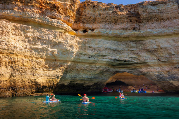 Tourists kayaking to Benagil Cave along Algarve coast in Portugal The Benagil Cave is one of the most beautiful destinations along the Algarve's dramatic limestone coastline. Tourists make their way to the cave through one of the arches. Photographed from a boat during a sunny Summer morning. benagil photos stock pictures, royalty-free photos & images