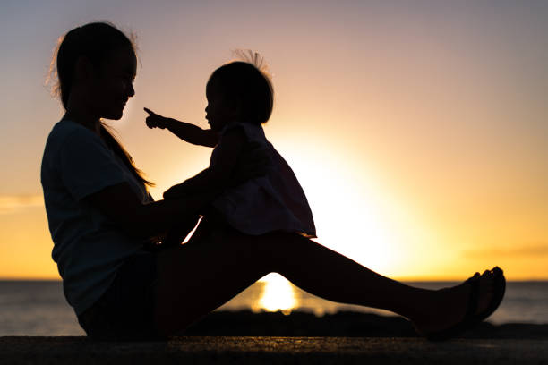 baby sitting on mothers lap with a orange sunset background, silhoutte.
