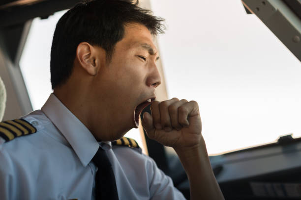 Tired man yawning at work. Pilot flying airplane. A male captain pilot sitting in the cockpit yawning while flying an airplane low quality of life stock pictures, royalty-free photos & images
