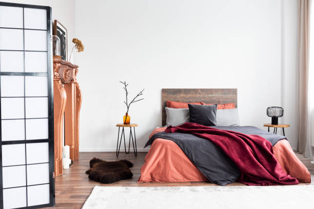 Copy space on empty white wall of rustic bedroom interior with king size bed with orange bedding and burgundy blanket