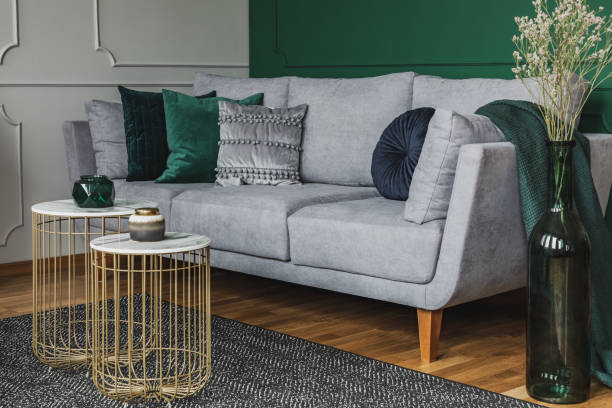 istock Two stylish small coffee tables with marble tops in front of elegant grey couch with emerald pillows 1176274881