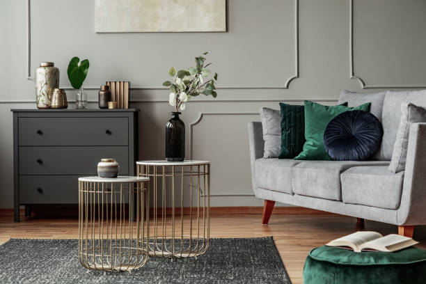 istock Two stylish small coffee tables with marble tops in front of elegant grey couch with emerald pillows 1176274895