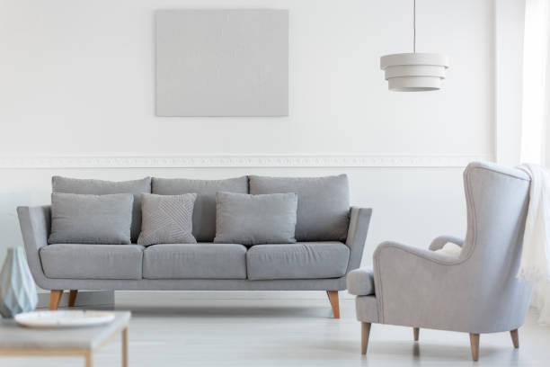 istock Big comfortable wing back armchair next to long grey scandinavian sofa with pillows in bright living room interior 1176274919
