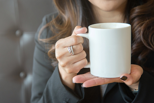 Young woman holding a white coffee cup with two hands outdoors and indoors.