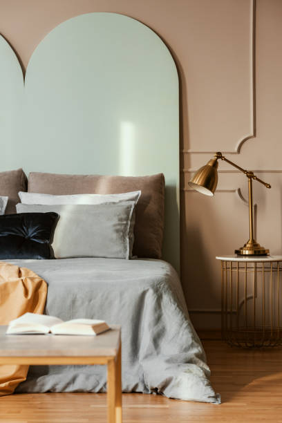 istock Golden lamp on modern nightstand table next to blue bed in grey bedroom interior 1176275770