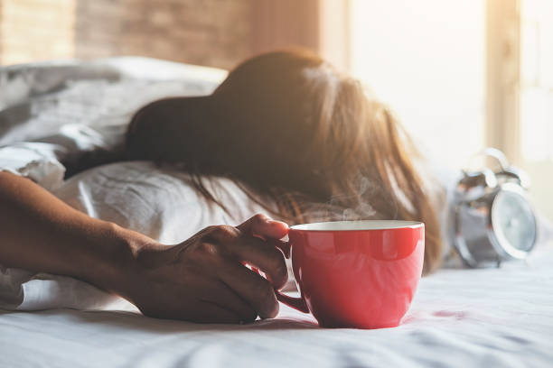 Beautiful asian female sitting in the bed with a cup of coffee. Morning with a book and cup of coffee. Relaxing concept. Beautiful asian female sitting in the bed with a cup of coffee. Morning with a book and cup of coffee. Relaxing concept. oversleeping stock pictures, royalty-free photos & images