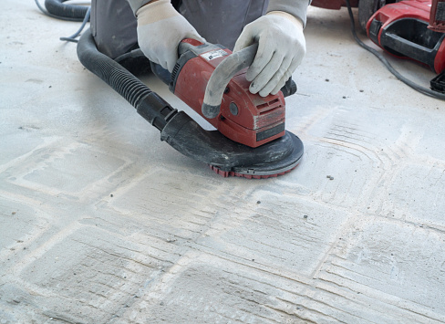 trabajador de la construcción utiliza una trituradora de hormigón para eliminar el pegamento de baldosas y la resina durante los trabajos de renovación photo