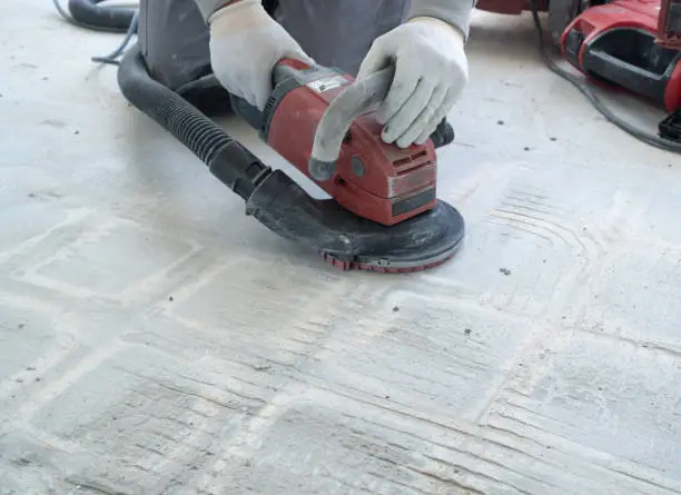 A construction worker uses a power concrete grinder for removing tile glue and resin during renovation work