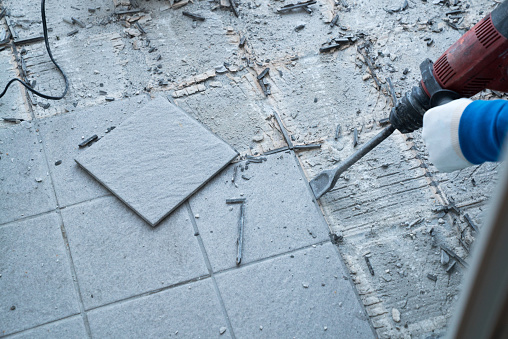 detail view of a construction worker using a handheld demolition hammer and wall breaker to chip away and remove old floor tiles during renovation work