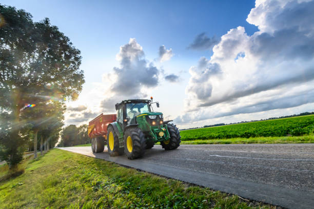 John Deere tractor hauling a tipper trailer on a country road in between agricultural fields stock photo