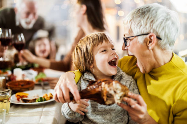 szczęśliwy chłopiec i jego babcia o jeść nogi indyka przy stole. - udziec z indyka zdjęcia i obrazy z banku zdjęć