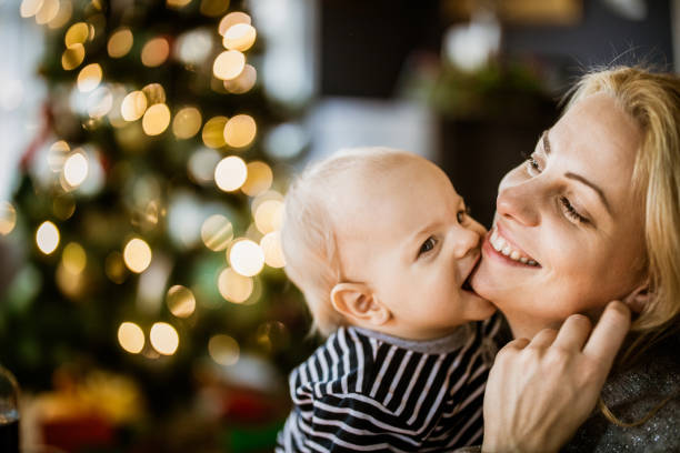 Happy mother enjoying with her baby son on New Year's day. Cute baby boy chewing mother's chin on New Year's day at home. baby new years eve new years day new year stock pictures, royalty-free photos & images