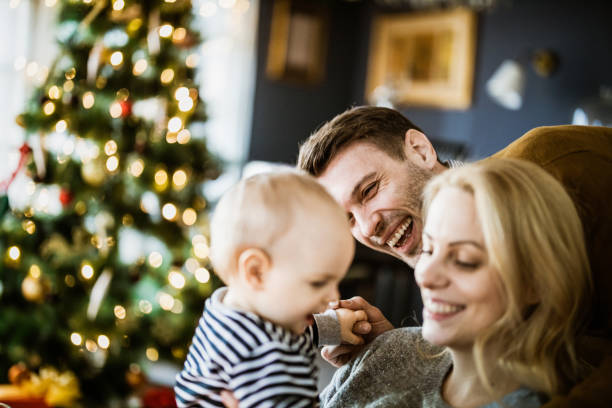 Young happy parents and their baby son during New Year at home. Happy parents having fun with their baby boy during New Year's day at home. Focus is on man. baby new years eve new years day new year stock pictures, royalty-free photos & images
