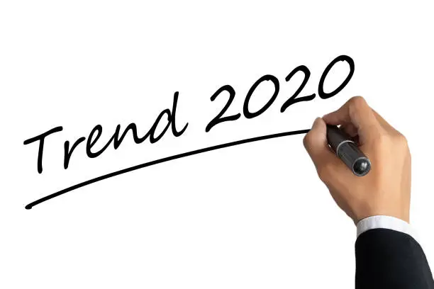 Photo of business man hand writing word trend 2020 with black color marker pen isolated on white background.TRENDS 2020 Business Concept