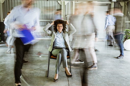Angry black businesswoman pulling her hair while being surrounded by her colleagues who are walking in blurred motion.
