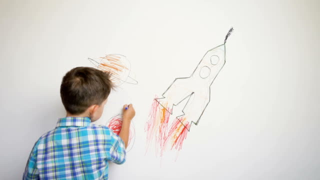 Boy drawing the rocket on white wall