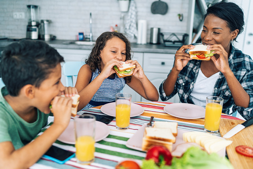 Modern afro-american mother with her two children eating sandwiches in the kitchen